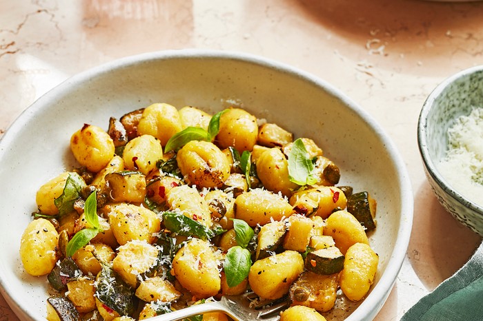 Two bowls of gnocchi on a table garnished with basil and grated cheese