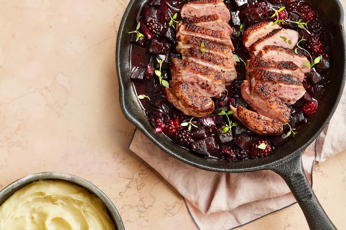 A cast iron pan with two sliced duck breasts surrounded by blackberries and chopped beetroot