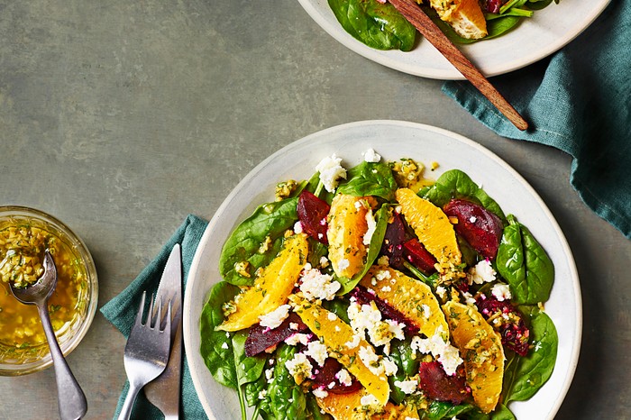 A white bowl filled with a beetroot, orange and green leaf salad with crumbled feta on top