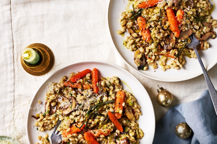 Two bowls filled with barley risotto and topped with orange roast carrots