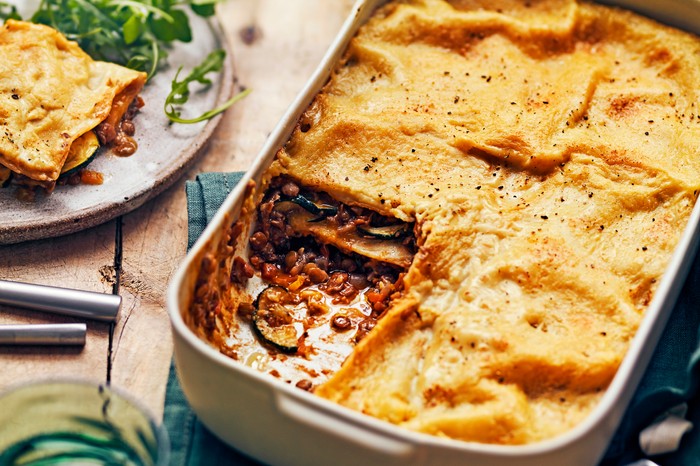 A golden vegan lasagne in a baking tray with one square taken out of it