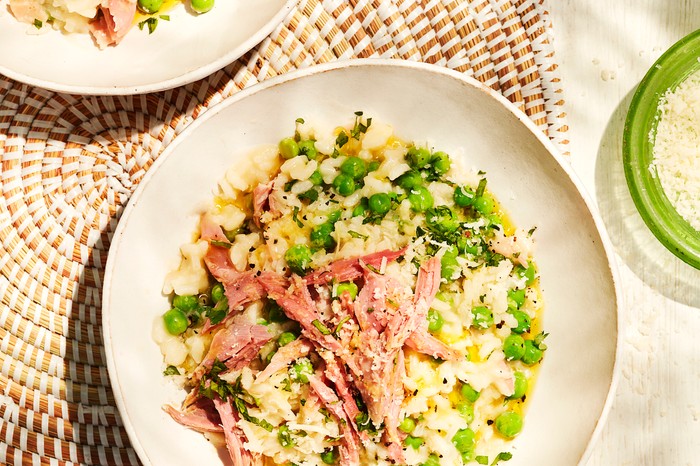 Two plates of risotto topped with peas and ham and resting on a weaved table mat