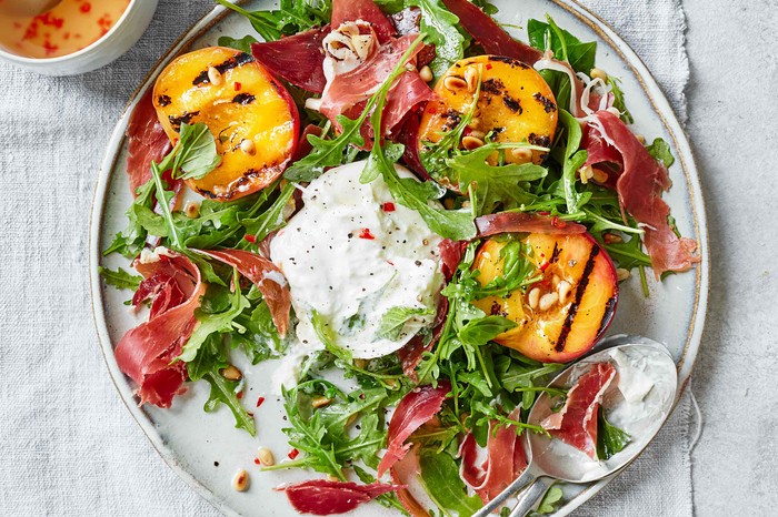 A grey plate topped with green leaves, orange peaches and a ball of white cheese