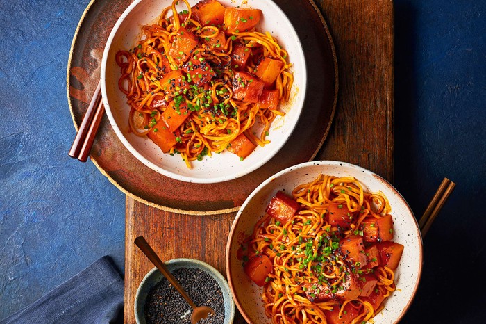 Two bowls of orange coloured noodles with chopsticks on the side