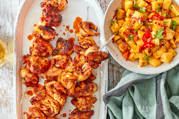 Paprika chicken kebabs on a plate, next to grilled pineapple chunks