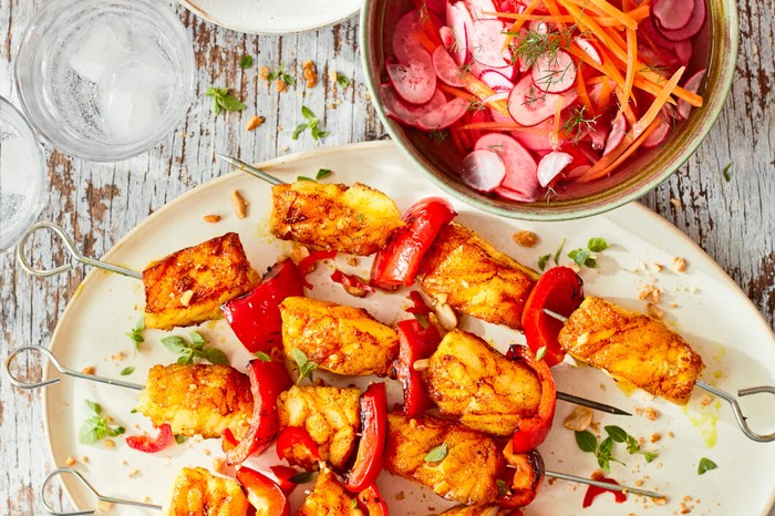 Turmeric fish kebabs with pickled carrot and radish salad on a large white plate