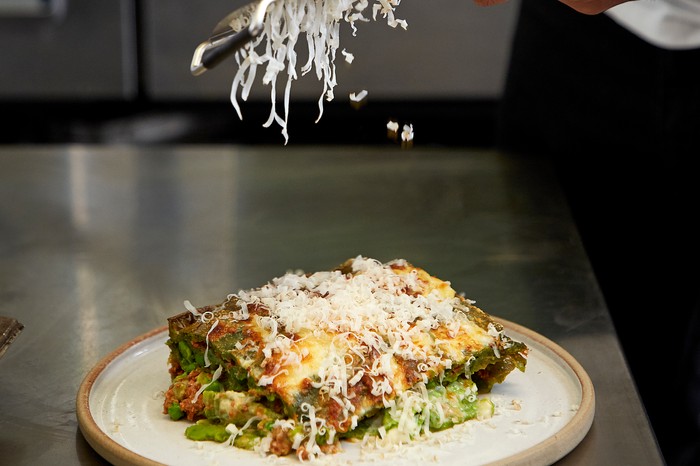 Grating parmesan over a plate of lasagne