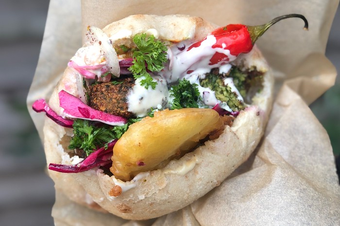 A pitta filled with falafel, cabbage salad, sauce, hummus and a fried potato slice