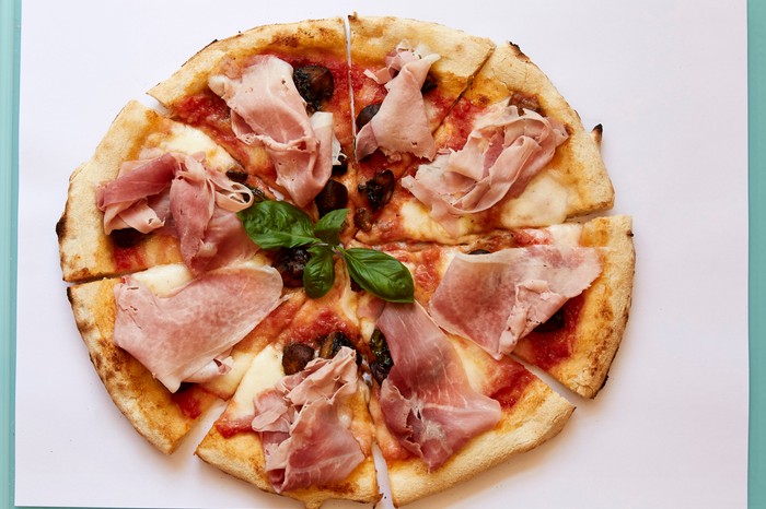 A pizza topped with tomatoes, fior di latte cheese, ham, mushrooms and basil