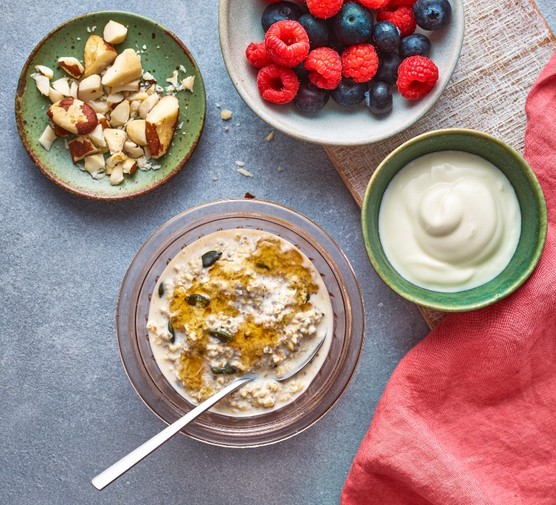 a bowl of oats next to plates of berries, yogurt and chopped nuts on a red napkin