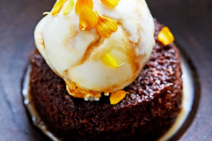 A dark circular sponge on a grey plate topped with a scoop of ice cream