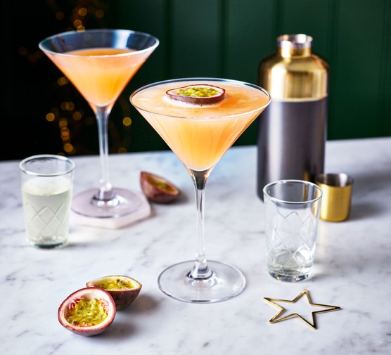 Two martini glasses filled with passion fruit martini, topped with passion fruit half