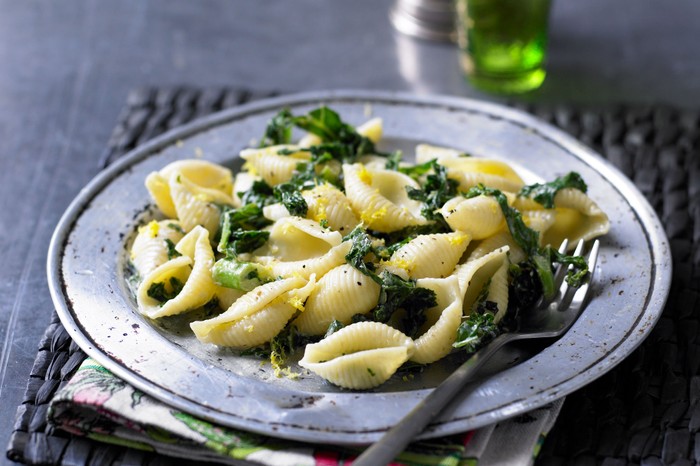 A grey shallow bowl filled with pasta, kale and anchovies