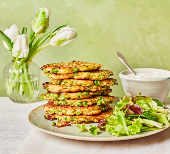 Pea and halloumi fritters with charred lemon dip Stack of pea and halloumi fritters next to a salad