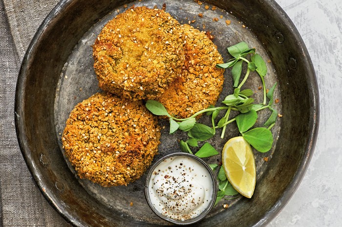 Pea fritters with some leaves, a wedge of lemon and pot of crème fraîche on a black plate