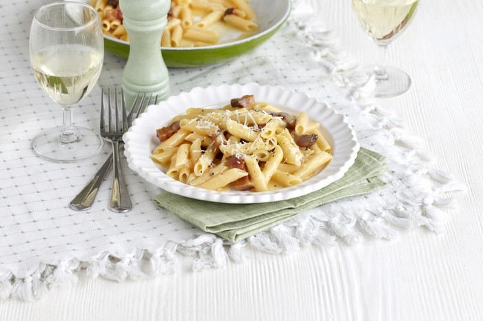 A plate of penne pasta with white wine on the side