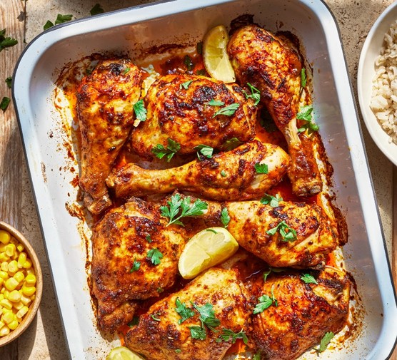 a silver oven tray filed with chicken topped with chopped herbs and lemon wedges