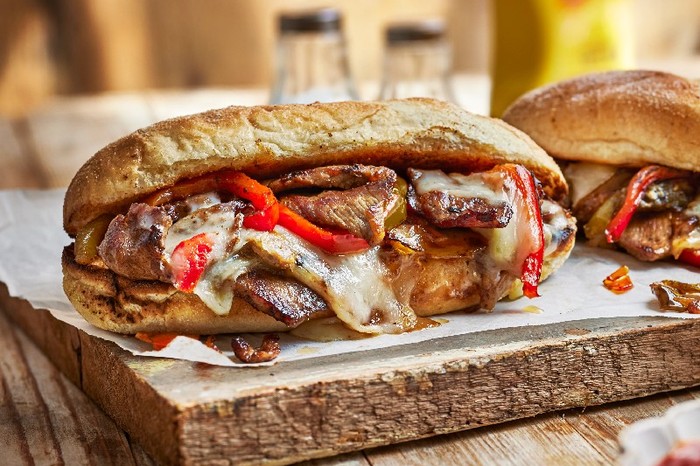 A sub roll loaded with steak, cheese and red pepper slices on a wooden board