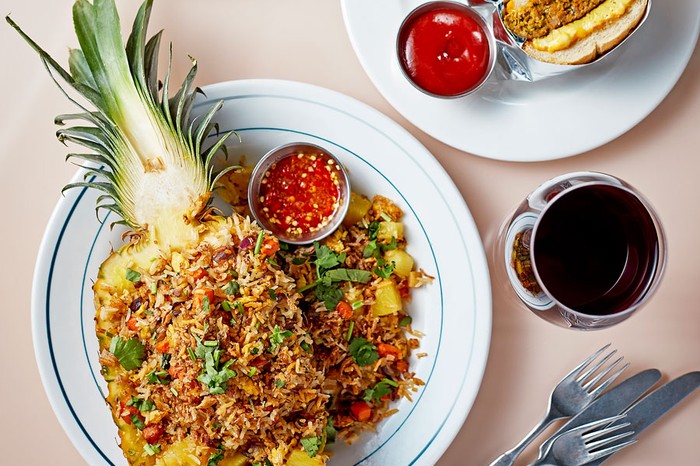 Pineapple filled with fried rice on a plate next to a ramekin of chilli sauce