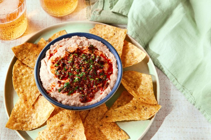 Dip in a small blue bowl with tortilla chips and drinks on the side