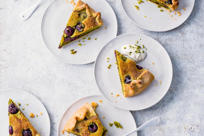 Bakewell Tart with Cherries and Pistachio galette cut up into triangles and served on round white plates on a rustic white table