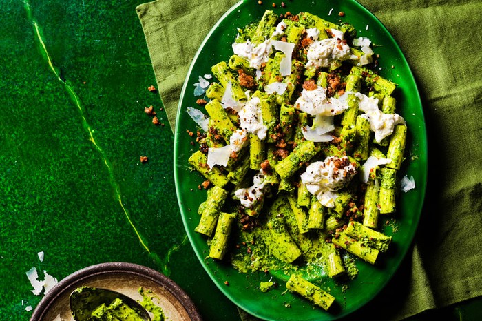 Green pasta on a green dish topped with burrata