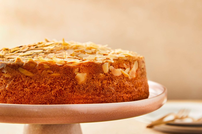 A round almond cake topped with almonds on a pale pink cake stand