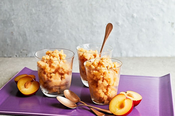 Three glasses of plum, ginger and sake granita surrounded by spoons and plum halves.