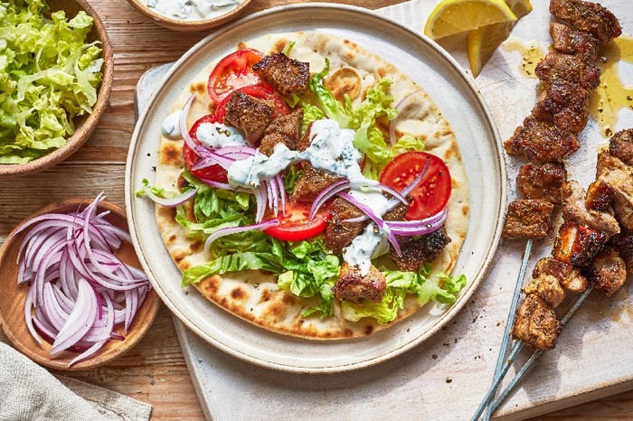 A round flatbreak on a plate topped with slices of pork, salad and a creamy sauce