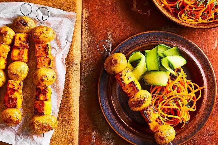 A plate of paneer skewers with cucumber and carrot salad next to a board of more skewers