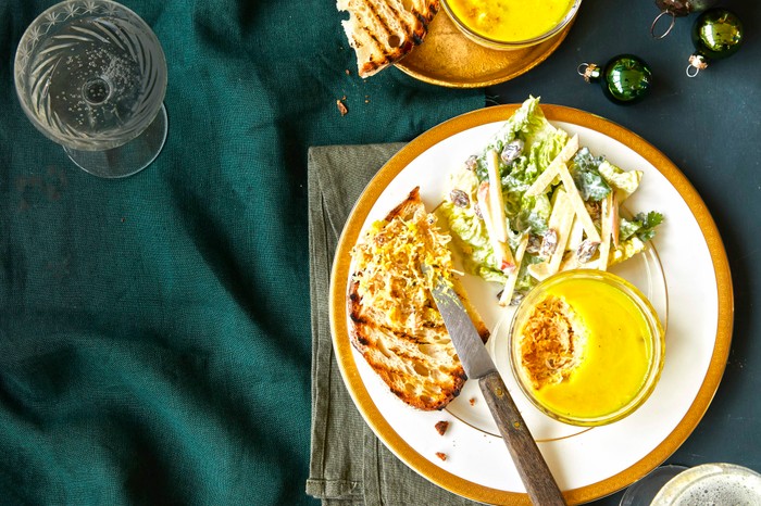 A white plate with a ramekin filled with crab, with a green salad and toast on the side