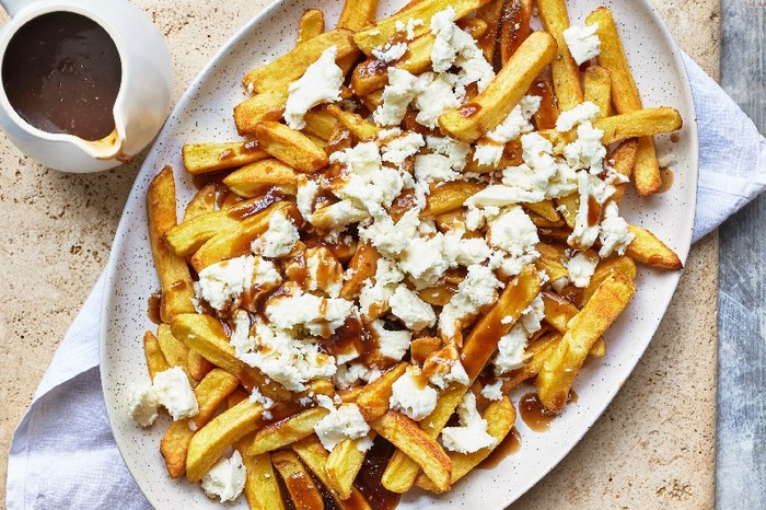 A white platter filled with chips topped with gravy and cheese, next to a small pot of extra gravy