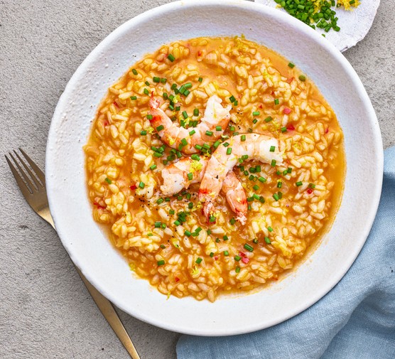 A bowl of prawn risotto topped with three large prawns