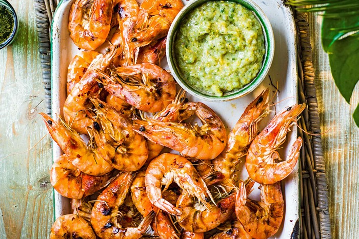 A silver tray topped with juicy pink prawns with a green sauce on the side