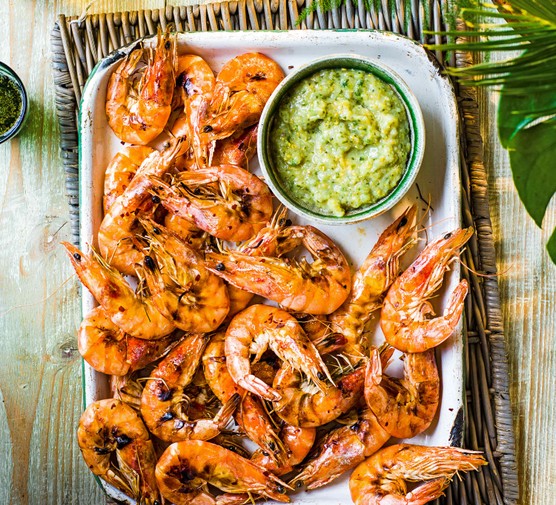 A silver tray topped with juicy pink prawns with a green sauce on the side