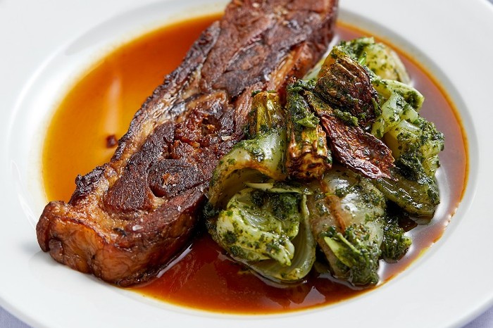 A slice of pressed lamb on a white plate with greens and gravy