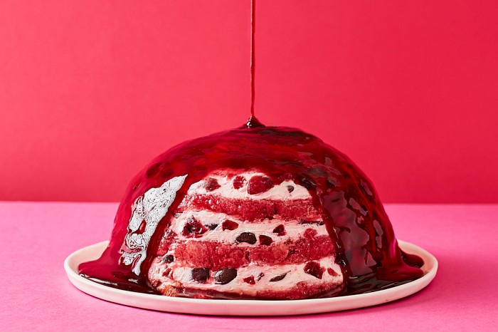 A round cherry pudding with sauce being spooned over the top