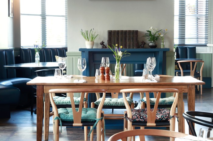 A dining room has a wooden table at the centre. There are pops of blue in the fireplace and furnishings