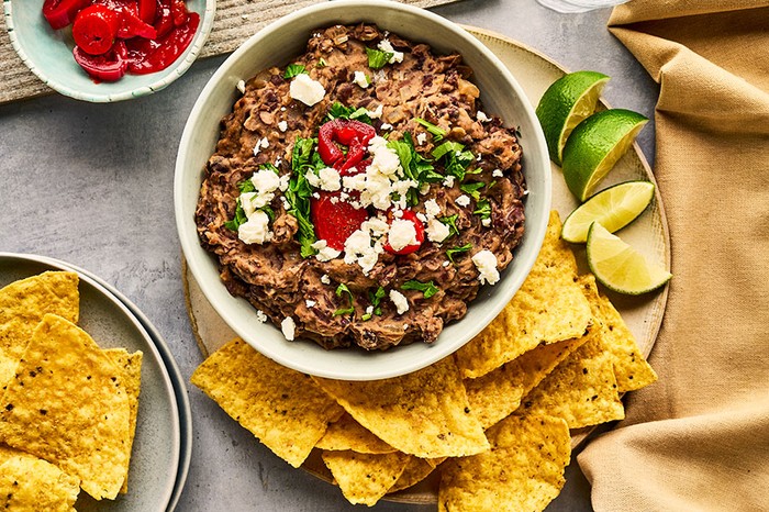 Bowl of refried beans topped with coriander, chilli and feta, with tortilla chips and lime wedges