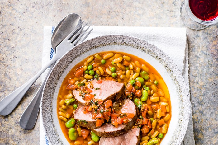 Lamb with Flageolet Beans Recipe served in a white and grey bowl and a glass of red wine