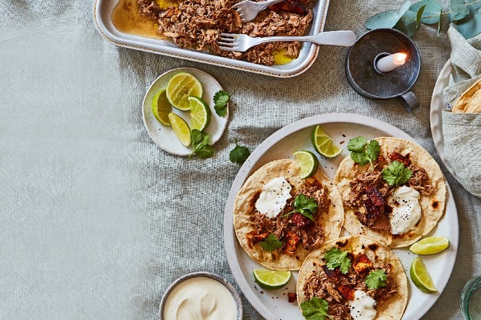 A tray of pork shoulder with cinnamon and clementines with three filled tortillas