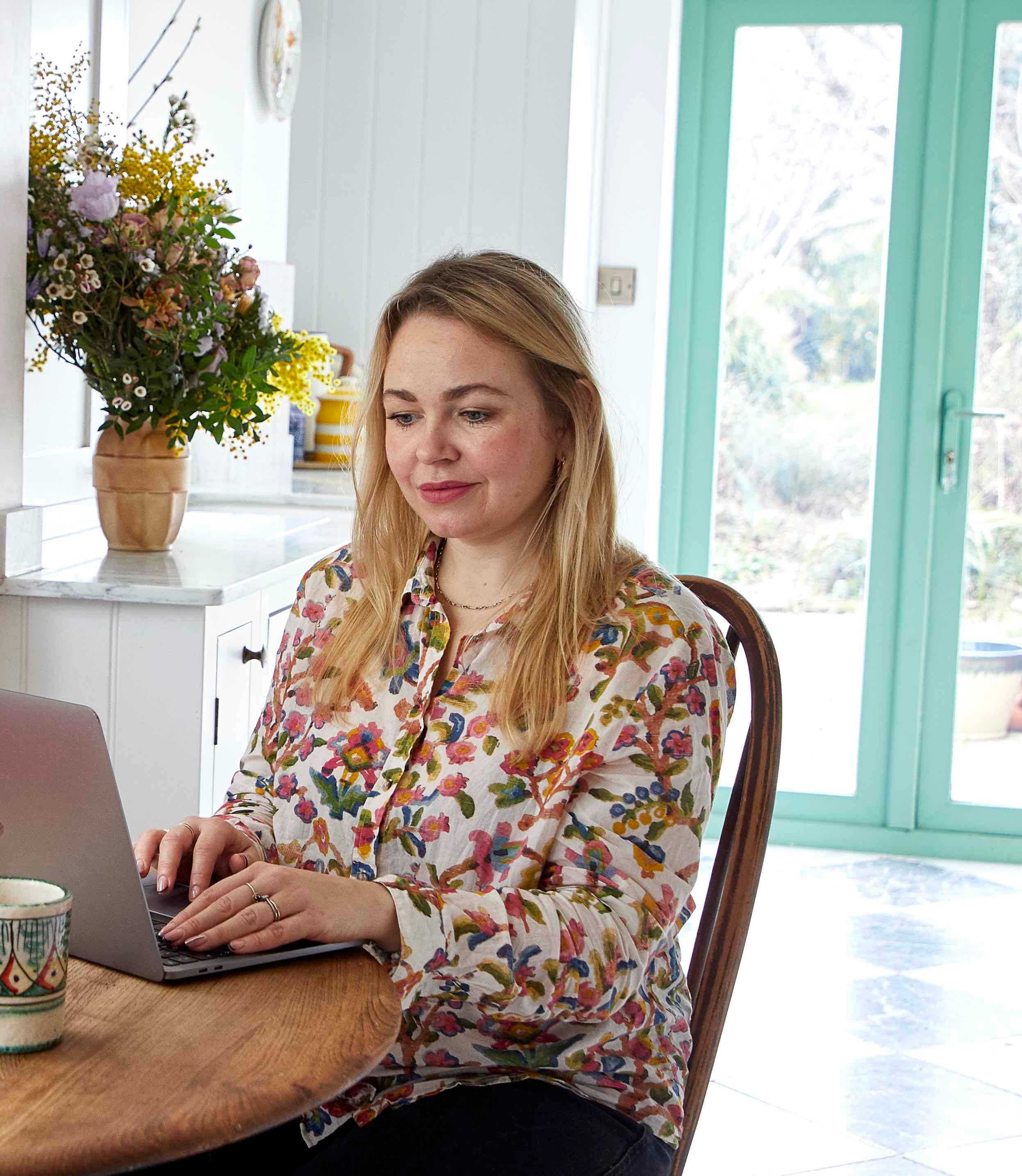 Rosie Birkett in a floral shirt sat at her desk