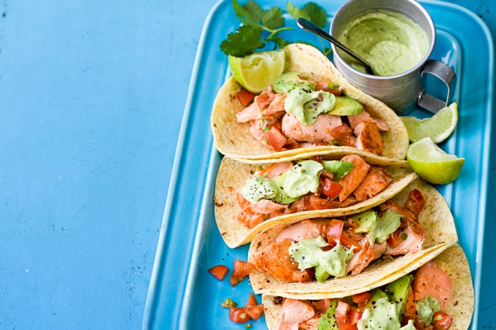 A tray of salmon tacos with avocado cream and limes wedges