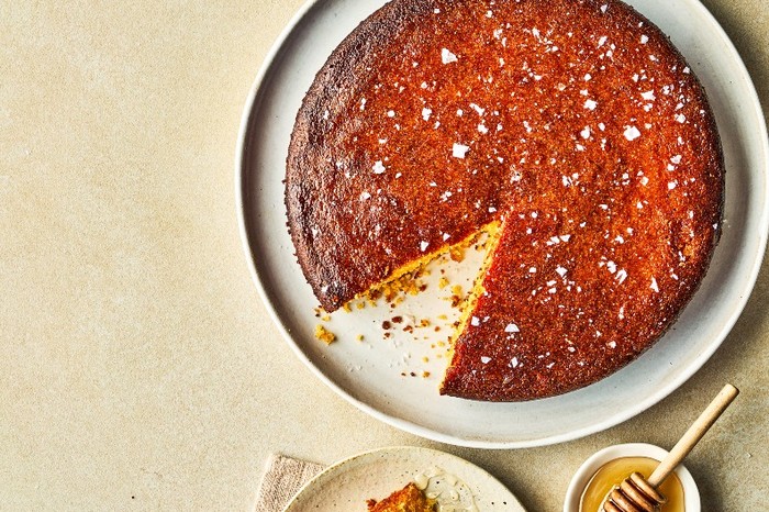 a golden-topped cake with flakes of salt next to a small bowl of honey and little pot of salt