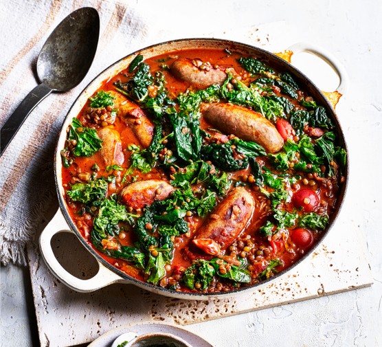 Pot of sausage and lentil casserole on a tea towel next to a spoon