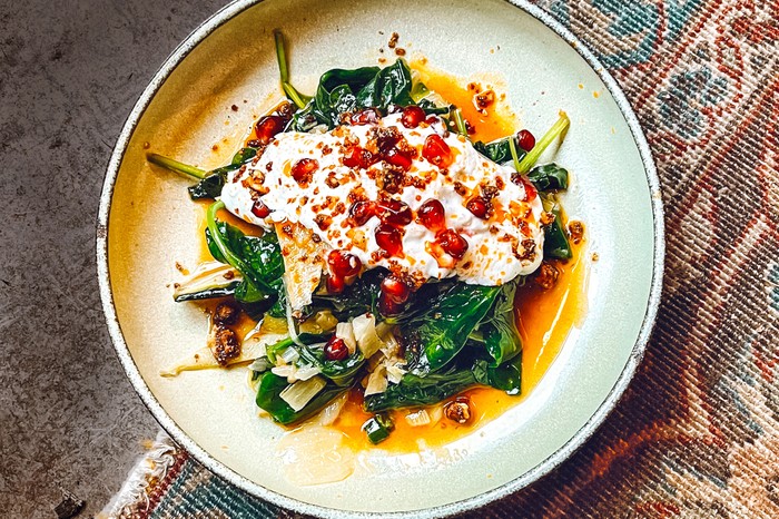 A plate of greens topped with Greek yogurt and pomegranate seeds