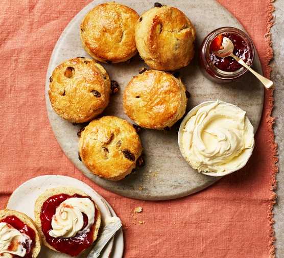 A plate of scones alongisde a pot of cream and a pot of strawberry red jam