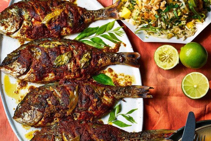 Barbecued fish on a platter with a side salad, laid out on an orange tablecloth