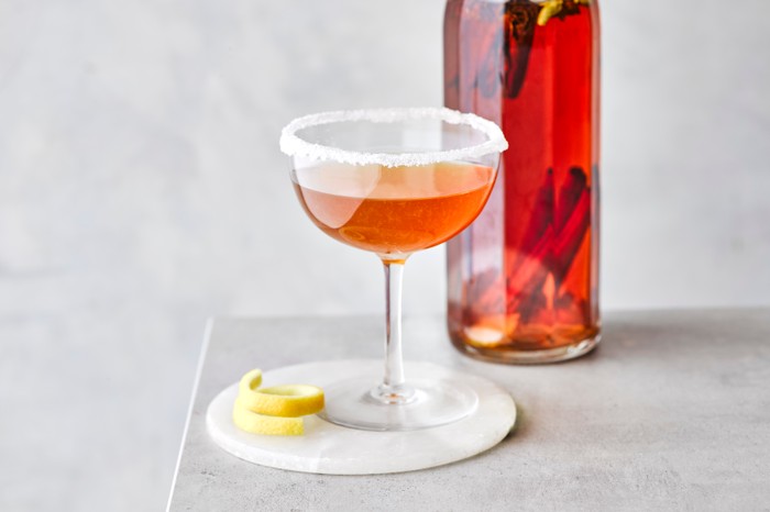 Sidecar cocktail in a coupe glass with a bottle of red liquid behind