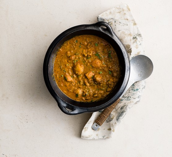 Pot of chicken curry next to a towel and metal spoon